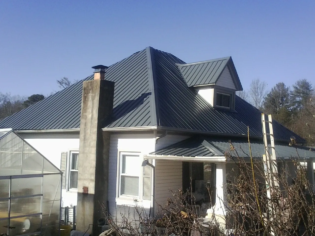 Dark blue standing seam metal roof on a white farmhouse with dormer — Slate & Tile Roof Repair by Roofing Brothers in Ackley
