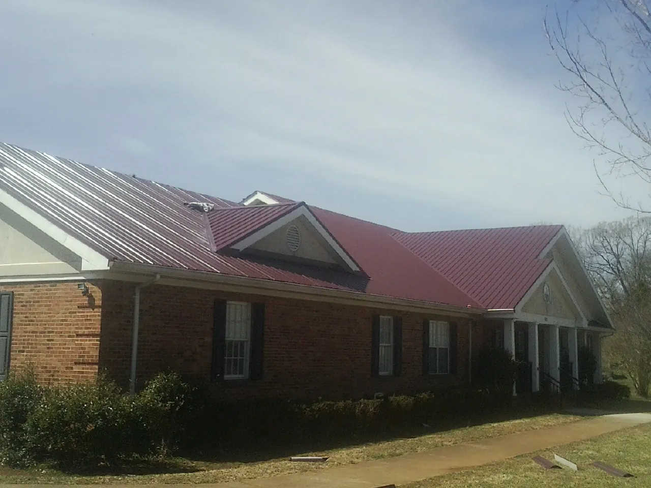 Red metal roof with gabled entries on a long brick building, from a Hail Damage Roof Repair job in Ackley