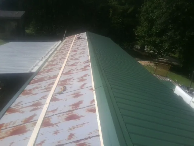 Old rusted panels beside newly installed green metal roofing — Wind Damage Roof Repair by Roofing Brothers in Ackley