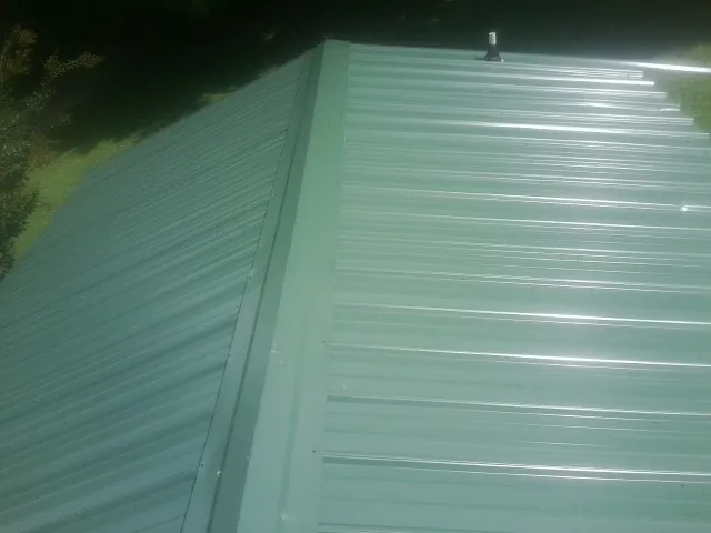 New green metal panels meeting at the ridge of a roof — Flat Roof Repair work by our crew in Ackley