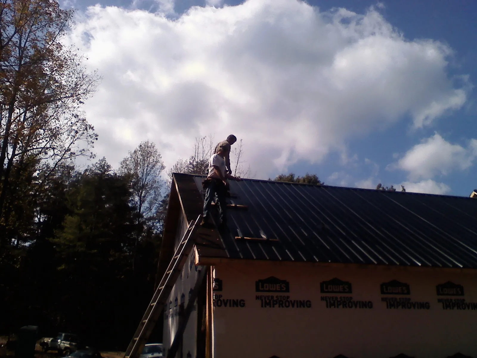 Roofer fastening dark metal panels high against a cloudy sky, from a Roof Inspection job in Ackley
