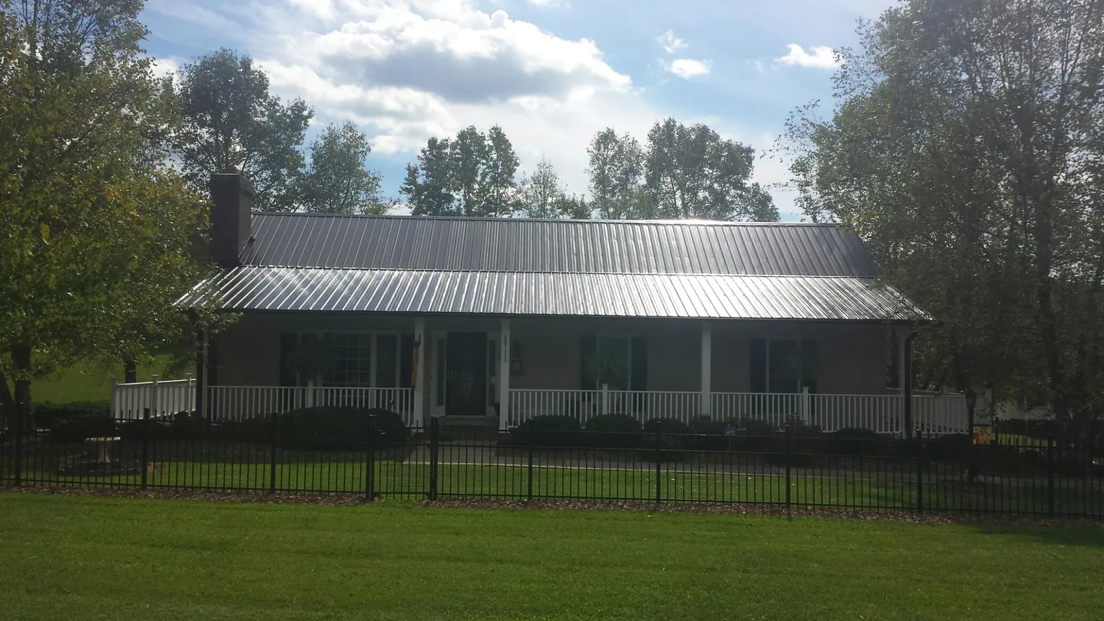Gray metal roof on a brick ranch with a full width front porch — Gutter Guard Installation work by our crew in Ackley