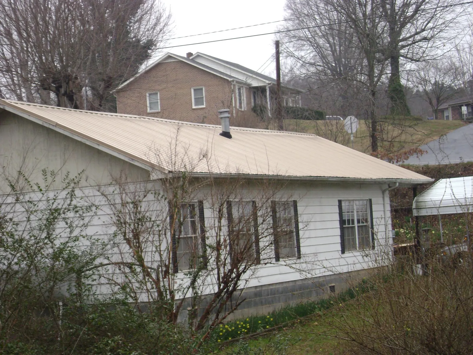 Tan metal roof on a white sided house set into a hillside in Ackley