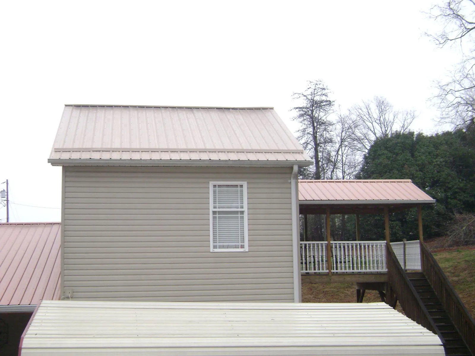 Tan metal roofs on a two story addition and attached porch, from a Roof Replacement job in Ackley