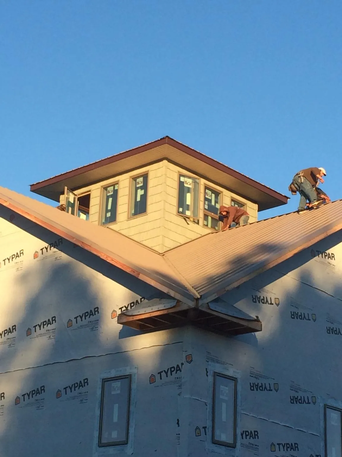 Roofers working around a rooftop cupola on a new metal roof at sunset — Roof Waterproofing in Ackley by Roofing Brothers